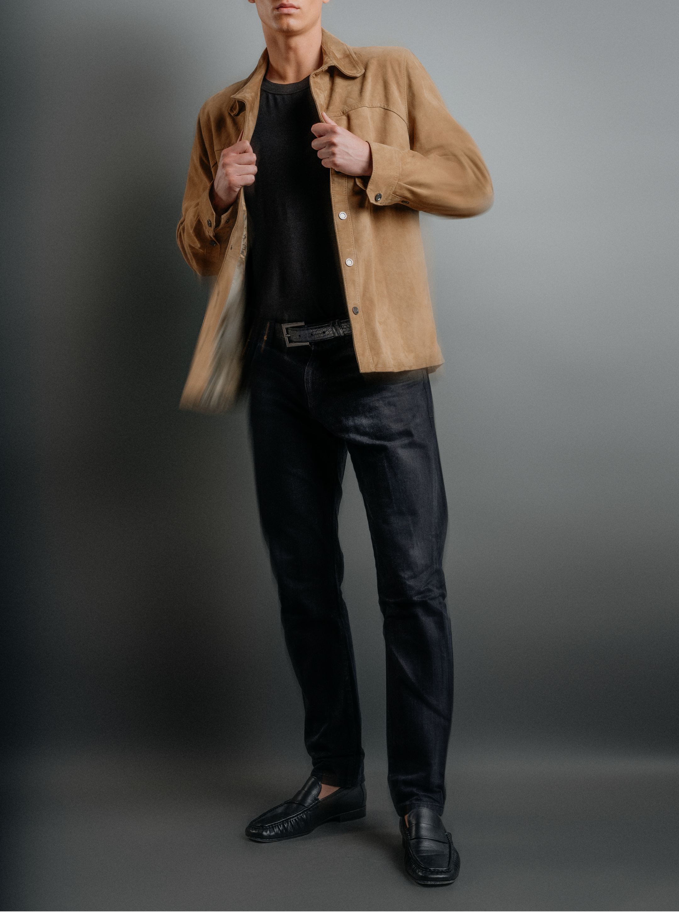 Man wearing a beige jacket over a black shirt and pants on a gray background